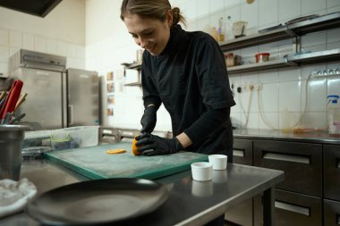 Young woman cuts an orange into circles to decorate a fruit salad, around the kitchen equipment
