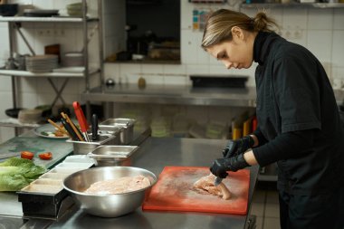 Woman chef cuts raw chicken fillet on a cutting board, she uses a professional knife