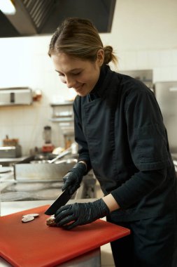 Woman chef cuts sous vide meat into thin slices on a cutting board, she uses a professional knife
