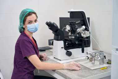 Woman laboratory assistant in a protective mask at the workplace in the laboratory, she uses modern equipment