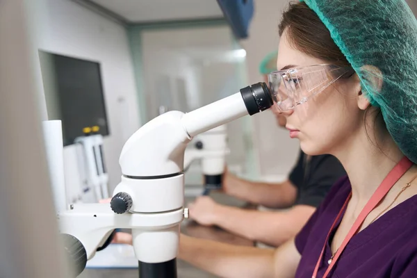 Female Laboratory Assistant Special Glasses Looks Microscope She Overalls — Stock fotografie