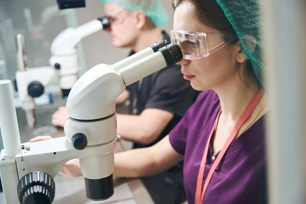 Laboratory staff in special glasses look through microscopes, they are in overalls