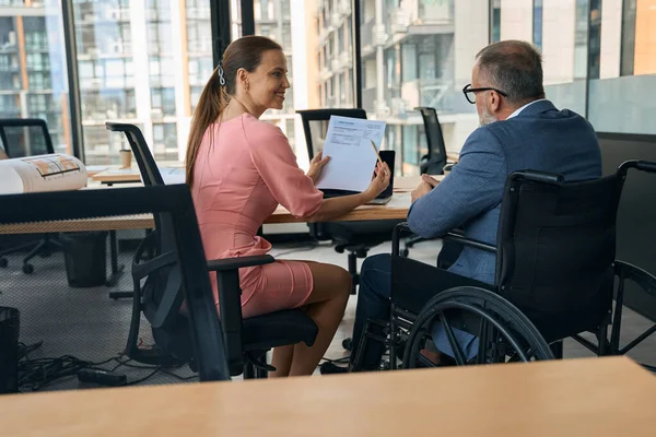 Businessman in a wheelchair and a friendly company employee in a modern office adjust working papers