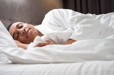 Cute multiracial man sleeps in bed on a soft pillow, he has sweet dreams
