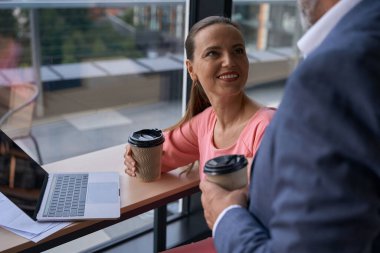 Colleagues, a man and a beautiful woman at a coffee break, they are located at a large window