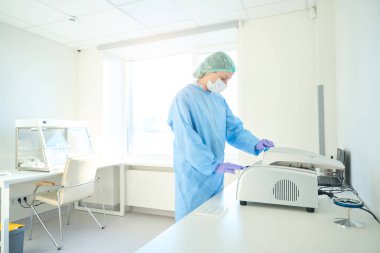 Hematologist in sterile overalls puts samples into a centrifuge, this is a modern diagnostic laboratory