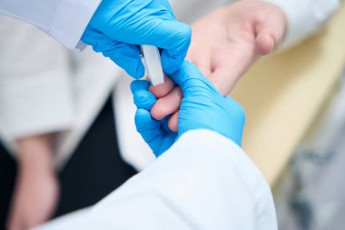 Health worker in protective gloves makes a finger puncture for blood sampling, a specialist uses a special needle