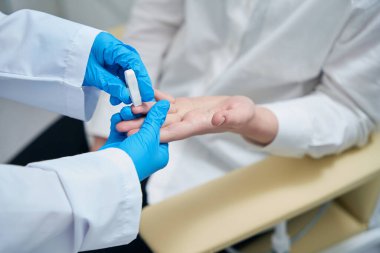 Health worker makes a finger puncture for blood sampling with a special needle, the manipulation takes place under sterile conditions
