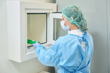 Virologist laboratory assistant transfers images of viruses from a sterile room to non-sterile one, woman in protective mask and overalls