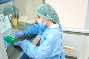 Laboratory employee works with virus samples in a sterile room, she is wearing a protective mask and gloves