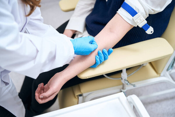 Лабораторный помощник вставляет иглу в вену пациента, медицинский работник использует защитные перчатки
