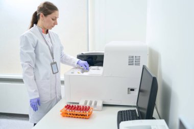 Hematologist laboratory assistant stands near an immunochemiluminescent analyzer in the testing unit of a modern laboratory