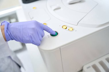 Laboratory assistant presses the button on the body of the immunochemiluminescent analyzer, the health worker in protective gloves