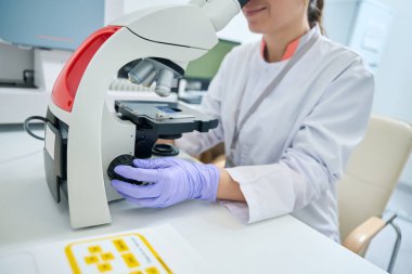 Geneticist examines under a microscope a sample of biomaterial for a DNA test, a woman works in a sterile room