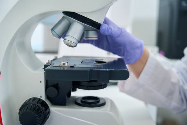 Laboratory employee works with a powerful microscope at the workplace, a specialist works in protective gloves