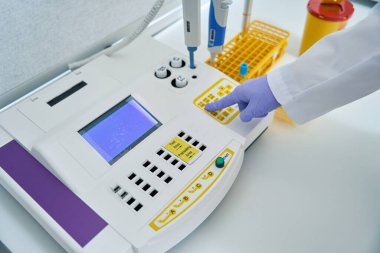 Employee of a diagnostic laboratory presses a button on a coagulometer, this device determines blood clotting