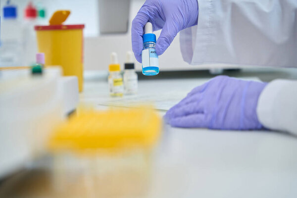 Blue liquid in bottle with pipette in hands of laboratory employee, this is a reagent for determining the blood type