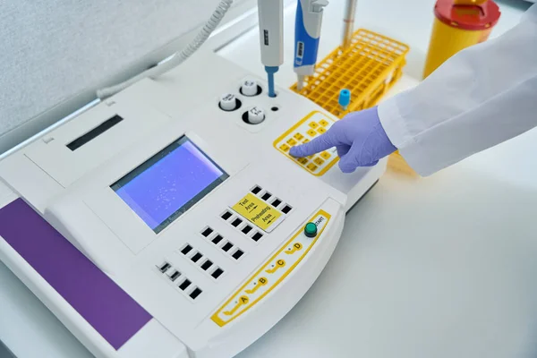 Employee of a diagnostic laboratory presses a button on a coagulometer, this device determines blood clotting
