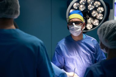 Kliniğin baş cerrahı. Ameliyathanede asistanları var. Cerrahi personeli var.