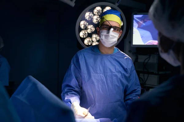 Team of doctors led by a leading surgeon at the workplace in the operating room, a powerful lamp indoors