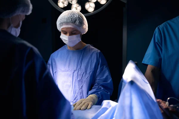 stock image Nurse in an operating uniform stands at the surgical table, next to her colleagues doctors