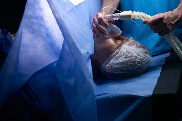 Woman lies on the operating table under anesthesia, the anesthesiologist holds a mask near her face