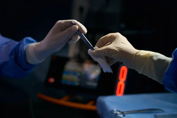 手术室里的外科医生把一个金属仪器交给一位同事 一位戴防护手套的助手 — 图库照片
