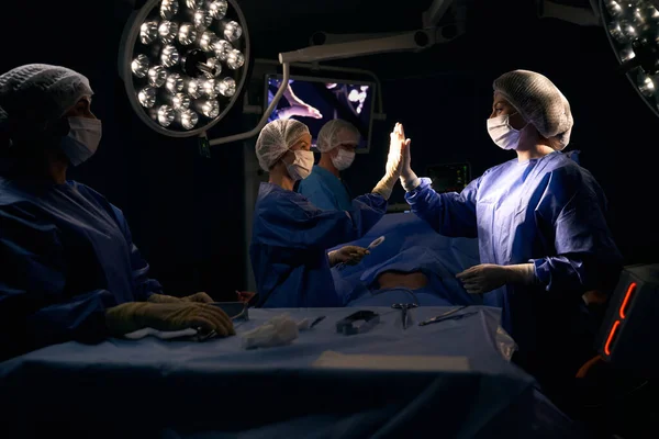 Colleagues surgeons give five after a successful operation, the patient lies on the operating table