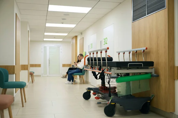 Ludzie Luźnych Ubraniach Siedzą Szpitalnym Korytarzu Pierwszym Planie Jest Łóżko — Zdjęcie stockowe