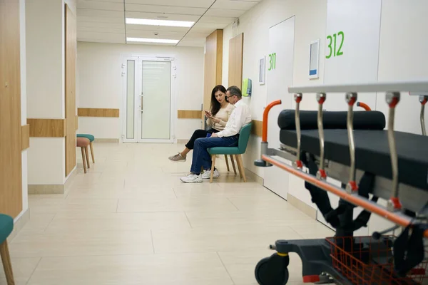 Ludzie Luźnych Ubraniach Siedzą Krzesłach Korytarzu Szpitalnym Pierwszym Planie Łóżko — Zdjęcie stockowe