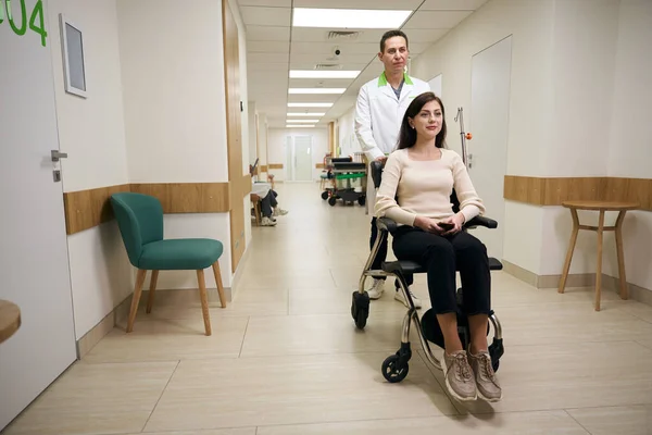 Άντρας Φόρμες Σπρώχνει Μια Νεαρή Γυναίκα Αναπηρικό Καροτσάκι Στο Διάδρομο — Φωτογραφία Αρχείου