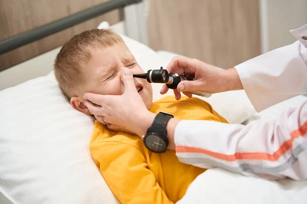 在诊所里 这个困惑的小男孩的近照正在被检查他的鼻子 — 图库照片