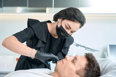 Koruyucu eldivenler ve maske takmış güzel bir doktor elinde şırıngayla yakışıklı bir erkeğe güzellik iğnesi yapıyor.