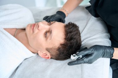 Koruyucu eldivenli profesyonel kozmetik uzmanı krem tutuyor ve salonda hasta yüzüne ilaç sürüyor.