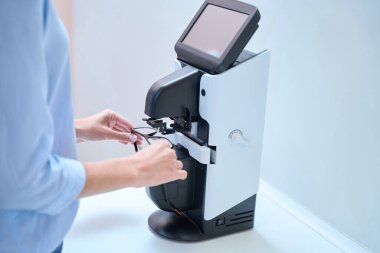 Tanınmayan kişinin yan görünüş portresi, gözlükçülerin kliniğindeki modern makineye koyarken el ele tutuştur.