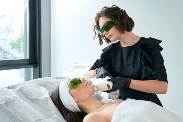 Jovem Fêmea Óculos Proteção Deitada Sofá Cosmetologista Perto Fazendo Depilação — Fotografia de Stock