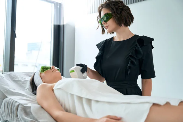 Senhora Óculos Proteção Deitada Sofá Cosmetologista Perto Fazendo Depilação Laser — Fotografia de Stock