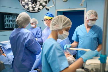Cerrahlar bir ameliyat yapar, anestezi altında bir hasta, doktorlar teşhis görüntülerini kullanır.