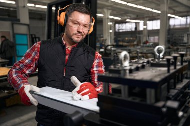 Koruyucu giysiler ve eldivenlerle gülümseyen erkek fabrikaya metal yapı kuruyor.