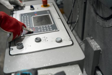 Koruyucu eldivenli bir erkek, fabrikadaki metal kesme aletlerinde fonksiyon seçiyor.