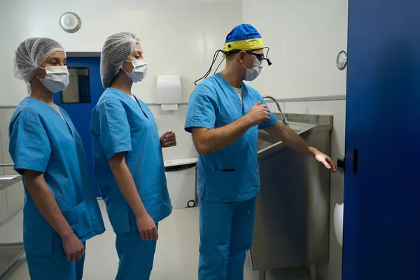 医生和他的助手们在手术前对双手进行消毒 医生们戴着防护面具 — 图库照片