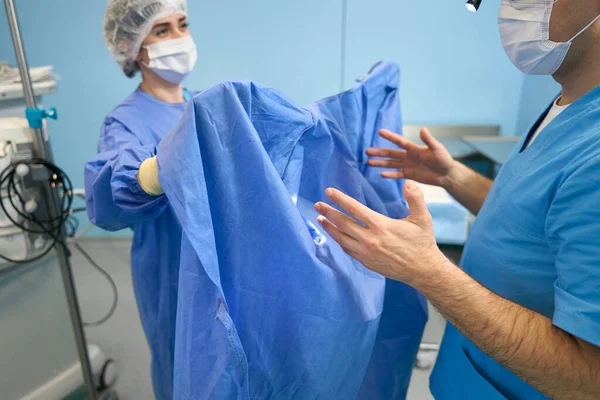 Asistente Sala Preoperatoria Ayuda Cirujano Ponerse Una Bata Médicos Con —  Fotos de Stock