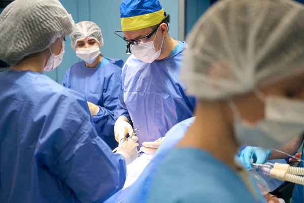 노란색 파란색 모자를 의사는 수술중에 클램프를 사용하고 환자는 마취중이며 요원들 — 스톡 사진