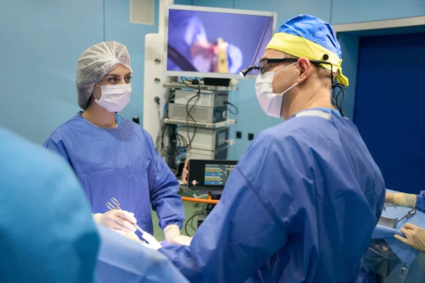 Surgeon with assistants operates on a patient in a sterile operating room, the process is demonstrated on a monitor