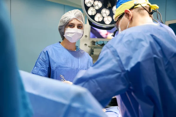 Female assistant holds a surgical clip in her hands, the surgeon works with a special camera