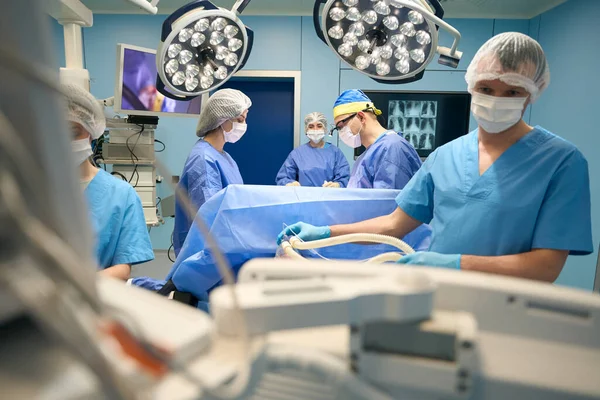 Anesthesiologist at work in a modern operating room, nearby his fellow surgeons are doing their part of the work