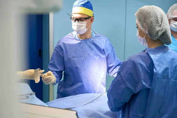 수술실에서 의료진 협동하여 일하고 보조자는 기구를 의사에게 건네준다 — 스톡 사진