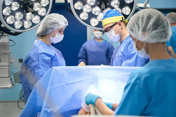 Modern operating room, medical teamwork, people work under powerful lamps in surgical gowns and protective masks