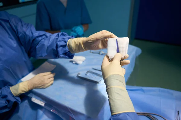 Assistant in the operating room passes the scalpel to the surgeon, people in surgical uniform