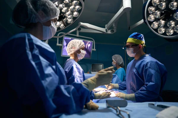 Team of doctors operates on a patient in a modern operating room, the patient under anesthesia lies on the table